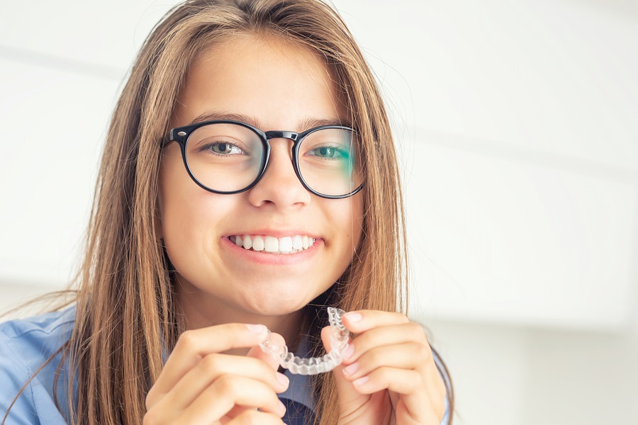 Smiling girl with glasses holding a clear aligner – From Overbites to Crowding