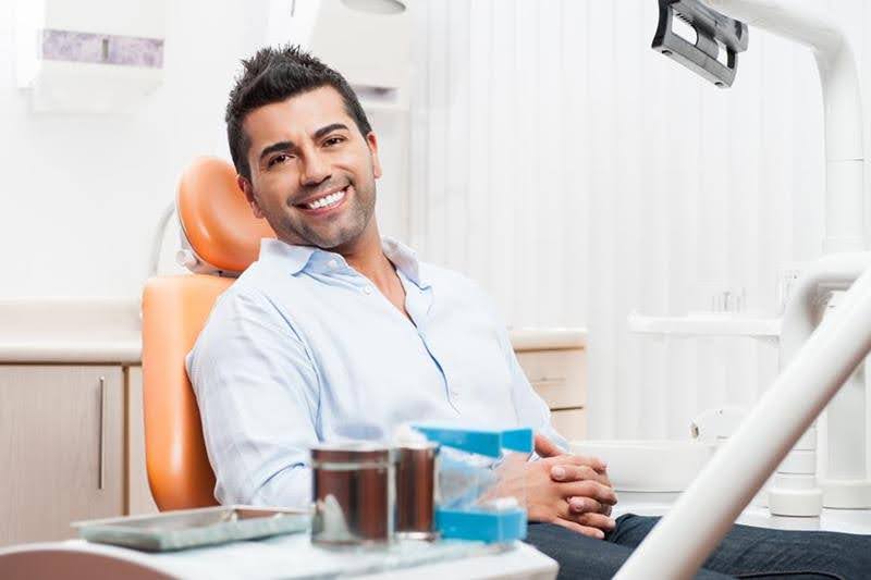 A happy, smiling male sitting on the dental chair at the dentist's office waiting for ozone treatment near him for his teeth. A happy, smiling male sitting on the dental chair at the dentist's office waiting for ozone treatment near him for his teeth.